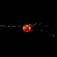 A fresh ripe red tomato with a green leaf flies in the air in water drops isolated on a black background. Concept of food levitation
