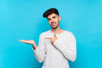Young man over isolated blue background holding copyspace imaginary on the palm to insert an ad