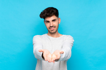Young man over isolated blue background holding copyspace imaginary on the palm to insert an ad