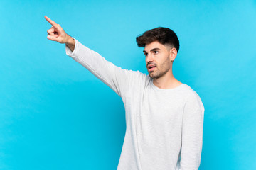 Young man over isolated blue background pointing away