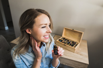 Young woman applying essential oils to her neck and holding bottle