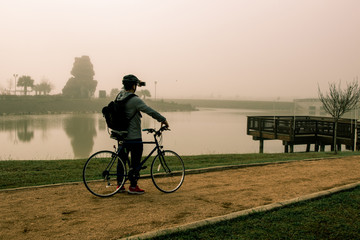 middle-aged man exercising on a bicycle in a park by a lake in the summer at sunrise