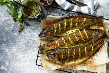Baked salmon fish with pesto sauce and culinary spices on a gray stone countertop. Top view flat lay background. Copy space.
