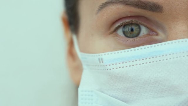 Single wonderful green eye of Russian doctor look forward isolated on white background close up. Portrait of young Caucasian woman in blue protective medical mask. Coronavirus covid-19 virus threat.