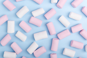 A bunch of white and pink marshmallow on a pastel light background. Colorful unhealthy sweets view from above. Blue texture backdrop sugar candies top view