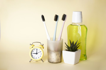 Toothbrushes in a glass and mouthwash with an alarm clock on a yellow background.