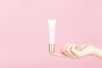 Unbranded flacon on female finger. Plastic tube for cream,body lotion, toiletry. Container for professional cosmetics product. Skincare and beauty concept. Mockup, copy space. Isolated on pink.