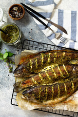 Baked salmon fish with pesto sauce and culinary spices on a gray stone countertop. Top view flat lay background.