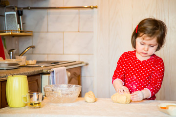 a cute little girl with blue eyes and red clothes is making cakes out of flour in the kitchen at home during the quarantine