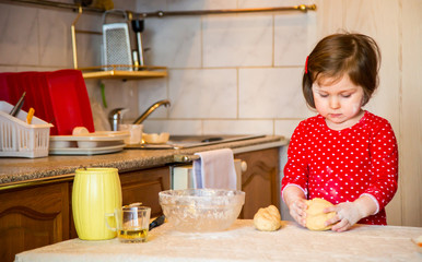 a cute little girl with blue eyes and red clothes is making cakes out of flour in the kitchen at home during the quarantine