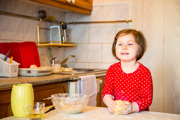 a cute little girl with blue eyes and red clothes is making cakes out of flour in the kitchen at home during the quarantine