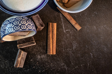 Close up of a bowl of sugar pieces of baking chocolate and whole sticks of fresh cinnamon ingredients 