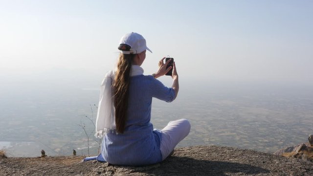 Girl with a smartphone takes a selfie on the top of a mountain