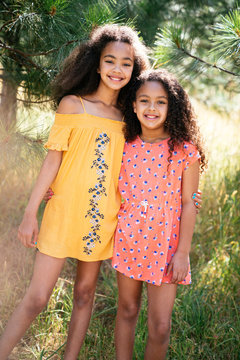 Portrait of smiling sisters in pretty summer dresses hugging outside in nature