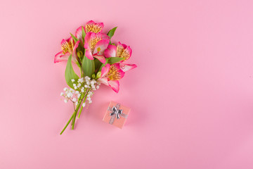 A bouquet of pink and white flowers and a small gift box on a pink paper background.