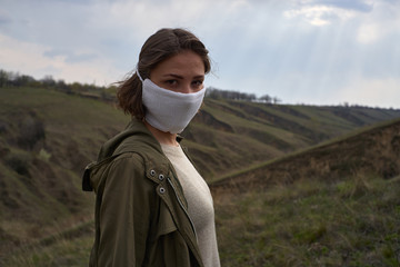 Girl in protective mask against the coronavirus on sky and nature background. World in post apocalypse after pandemic covid-19, quarantine and global catastrophe