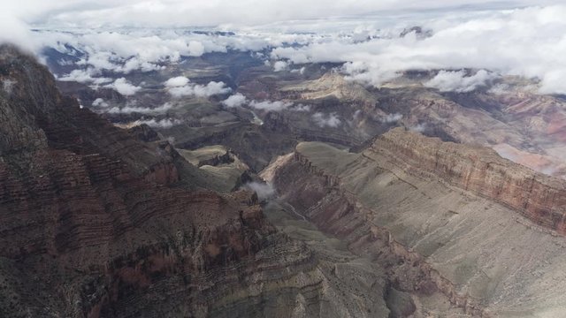 A wide timelapse looking west of clouds flowing inside the Grand Canyon. Clouds pass the camera temporarily obscuring the frame before moving on to reveal the canyon far below.