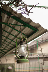Green rustic retro  petroleum lamp 
hanging from the roof in a courtyard