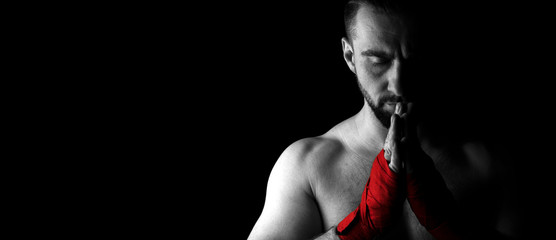 Banner image of a man’s fighter with a beard and red bandages on his hands. Hands are folded for prayer and eyes are closed. Black white image with red. Place for text. Black background.