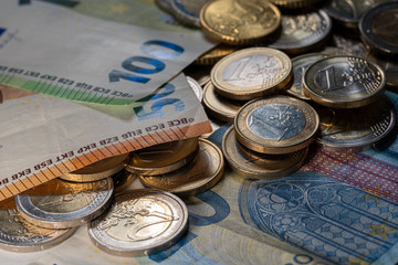 Euros in coins and banknotes, shiny euro on top of one hundred euro bill.