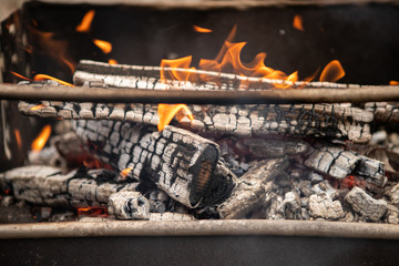 Flaming log (wood) in a metal outdoor brazier with ashes and smoke in rural courtyard