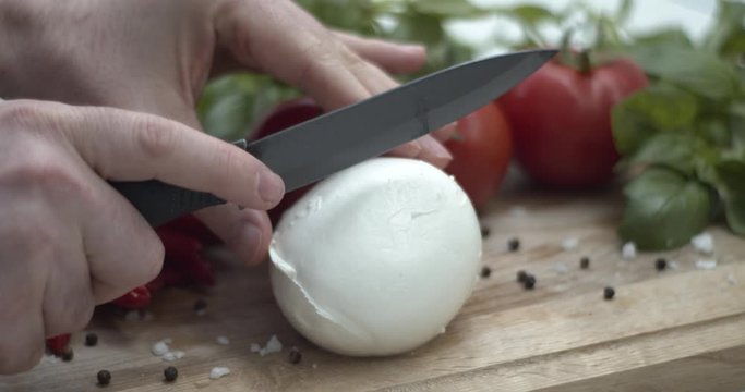 Tagliare una mozzarella di bufala sul tagliere per preparare una caprese: ricetta italiana