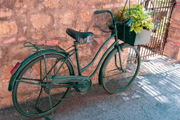 Fototapeta na wymiar retro bicycle with basket with green plants on the street in village in Tuscany