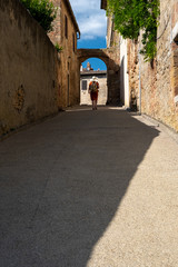 a young woman with hat and traveler backpack on a narrow street with an arch on a sunny summer day in Tuscany, Italy