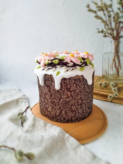 Easter cake decorated with a wreath of pink cream flowers and white glaze, on a light background close-up view from the side. Festive pastry.