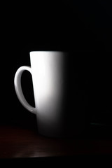 Taza de café blanca y caliente saliendo humo en la oficina de casa y mano que la sujeta para tomar  un sorbo 