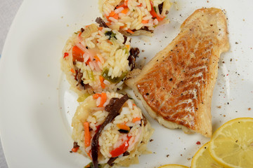 colorful rice with vegetables and fried fish on a white plate