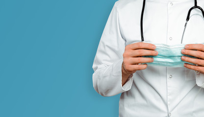 The doctor in a white coat on a blue background puts on a face mask. Medical and pharmaceutical concept. Medical service in the fight against diseases and the threat of an epidemic, pandemic.