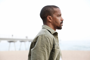 Fototapeta premium Side portrait of black young man walking on beach towards water. Outdoor.
