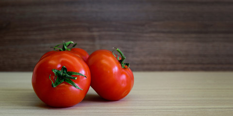 Three red fresh tomatoes on a wooden table.