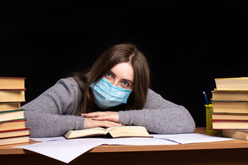 a young girl in a medical mask bowed her head on books. training during quarantine. remote work....