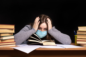 a girl in a medical mask sits bent over a bookstore and holds on to her head. emotions: fright, tired, sadness.