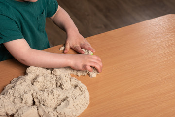little boy plays kinetic sand on the table. hands closeup. leisure at home.