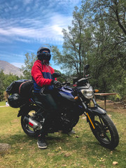 Fototapeta premium Guy with red and blue jacket and black motorcycle and helmet at chilean countryside, Cajón del Maipo, Chile