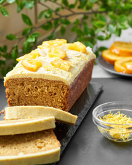 Vegan orange loaf cake and  slices.Homemade citrus cake with white cashew cream on top. Green spring leaves around.