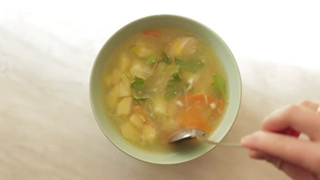 plate of cheap simple soup stands on white table similar to a table in dining room and female hand with a spoon stirs the soup