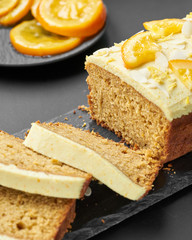 Vegan orange loaf cake and  slices.Homemade citrus cake with white cashew cream on top. Green spring leaves around.