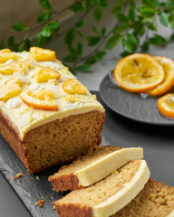 Vegan orange loaf cake and  slices.Homemade citrus cake with white cashew cream on top. Green spring leaves around.