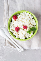 Homemade cottage cheese with raspberry and mint in a bowl. Russian homemade cottage cheese. Light grey concrete background.