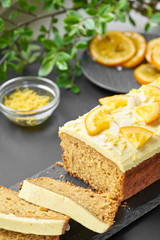 Vegan orange loaf cake and  slices.Homemade citrus cake with white cashew cream on top. Green spring leaves around.