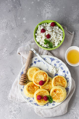 Cottage cheese pancakes, syrniki with honey, raspberry and mint on ceramic plate and homemade cottage cheese in a bowl. Healthy breakfast or lunch. Top view.