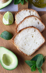 Sliced homemade no knead bread on wooden cutting board with avocado. The concept of homemade bakery without yeast. Light grey stone background. Top view.