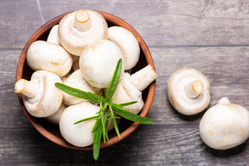 Fresh raw champignons in a clay bowl on wooden rustic background top view. Healthy diet food concept.