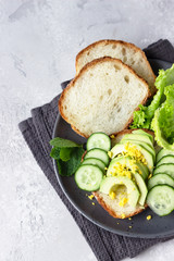 Healthy vegetarian sandwich with no knead homemade bread, avocado and cucumbers for breakfast or lunch. Light grey stone background. 