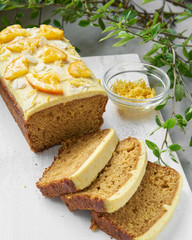 Vegan orange loaf cake and  slices.Homemade citrus cake with white cashew cream on top. Green spring leaves around.
