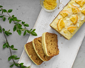 Vegan orange loaf cake and  slices.Homemade citrus cake with white cashew cream on top. Green spring leaves around.